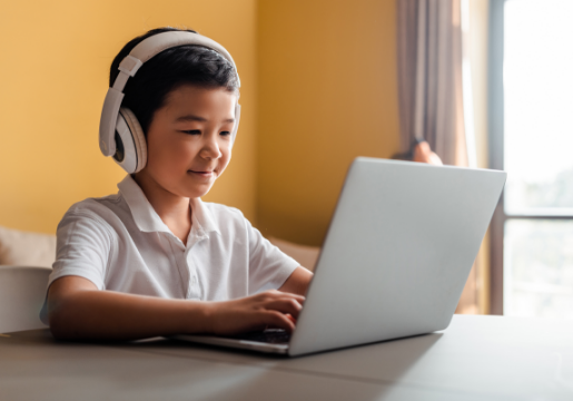 Young boy with white headphones and polo shirt working on a laptop